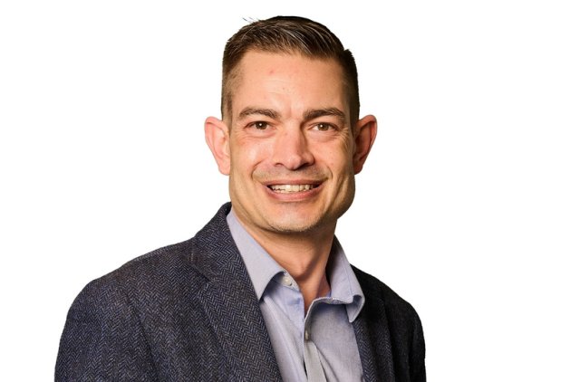 A professional headshot of Dominic, smiling into the camera in a suit